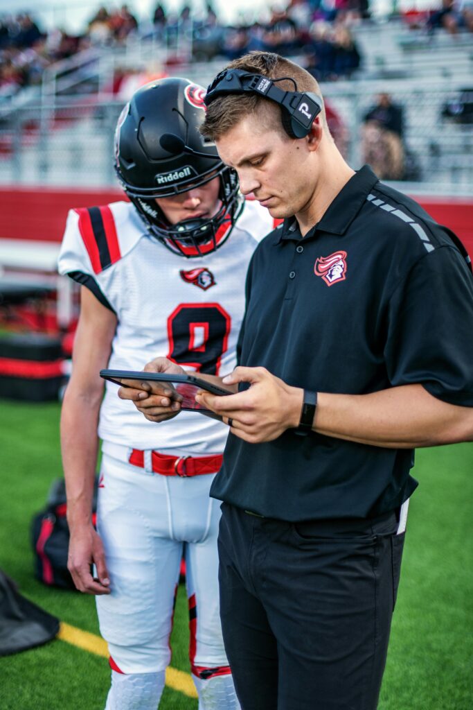 A football coach and player review plays on a tablet during a game.